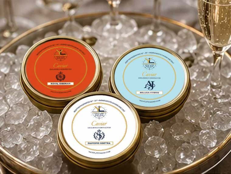 Three Yacht Life Caviar tins on crushed ice with custom labels in coral, pale blue and ivory, showing a monogram and family crests, beside a glass of champagne